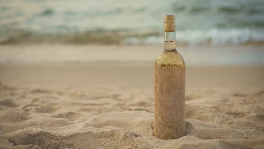 Vintage bottle of white wine on sandy ocean beach with copy space close up. Picnic at seashore during summer evening