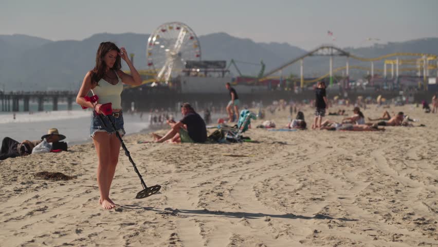 Female With Metal Detector Searching For Valuables in Sand of Santa Monica Beach CA USA