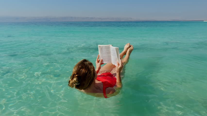 Young Woman Reads while Floating in the Dead Sea in the Jordan Rift Valley.