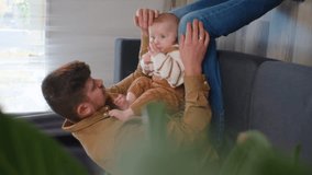 Vertical video of happy loving young dad with pretty little baby son sitting on comfy sofa at home, tiny toes of newborn child. Tender moments with kid, father and offspring connection, care concept