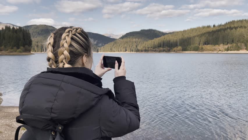 Woman With A Mobile Phone Taking A Picture Of Bolboci Lake In Romania. Close Up