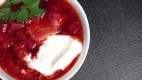 A bowl of borscht with a leaf of parsley and sour cream on a black background. View from above. Very close-up. Home cooking. Cooking master class. Video recipe for making borscht. Copy space.
