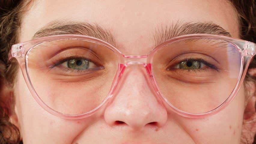 Young attractive brunette woman with curly hair in a bun wearing pink glasess close-up, white background. Portrait