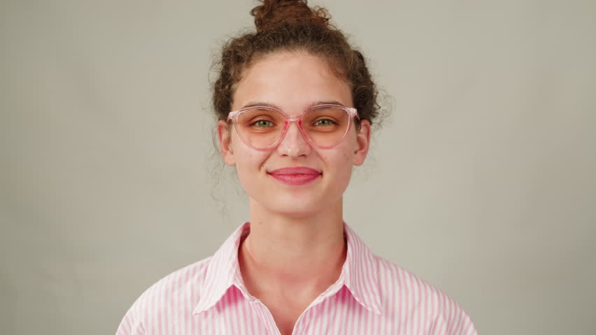 Young attractive brunette woman with curly hair in a bun wearing pink glasess close-up, white background. Portrait