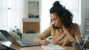 Young multi racial woman working remotely at home office looks at laptop computer, e learning online on internet website. Concentrated focused african female student makes notes in work document 4K - Powered by Shutterstock - Get 15% off with code: PIKWIZARD15