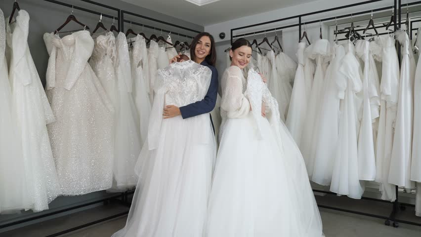 Portrait of two happy brides in a wedding salon with wedding dresses in their hands. Two women choose a wedding dress. Royalty-Free Stock Footage #1111232281
