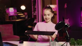 Kid content creator filming keyboard review in home studio, pressing different buttons to show typing capabilities. Little girl showcasing computer peripherals to audience on gen Z online channel