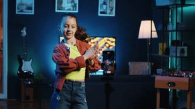 Little girl doing nice dance moves, filming viral challenge using smartphone. Happy kid having fun recording video with mobile phone for online fans in dimly lit home studio