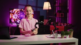 Child filming video with phone attached to selfie stick for online channel, talking with viewers. Kid telling audience topics she wishes to explore in future clips, recording with cellphone camera