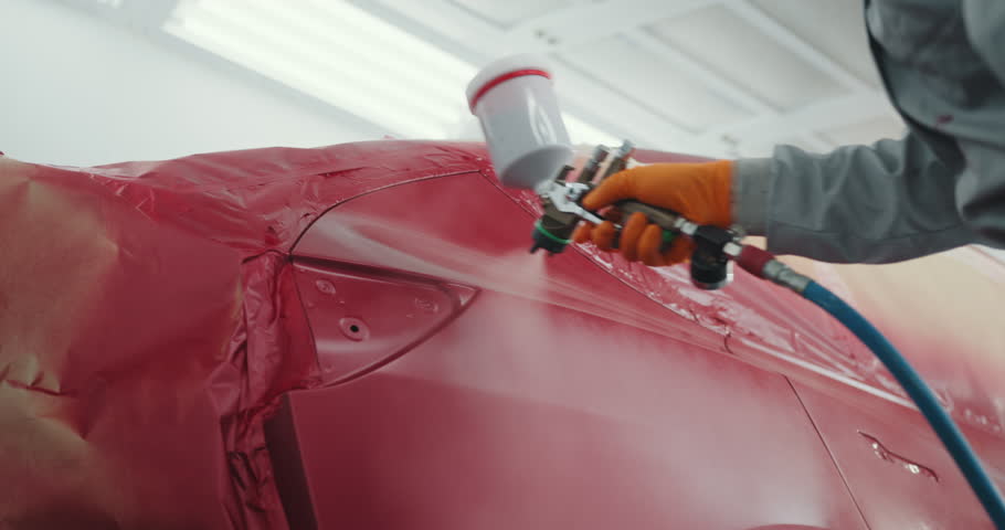 Auto painter spraying red paint on car door in special booth. Painting vehicle parts at car service workshop. Car manufacturing factory. Automotive paint services, quality auto body shop concept