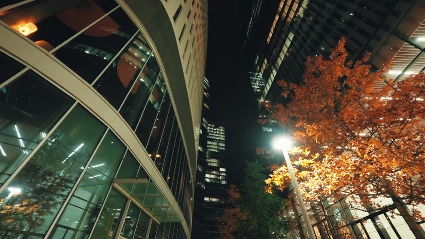 Low angle dolly shot illuminated skyscrapers cityscape at night, financial district looking up modern architecture office buildings, city business center downtown, gimbal shot, Warsaw evening street
