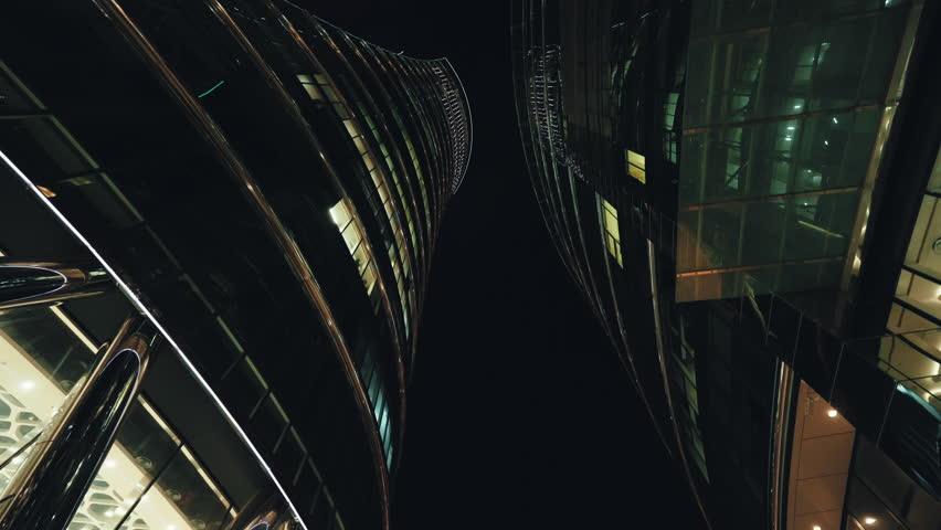 Low angle dolly shot illuminated skyscrapers cityscape at night, financial district looking up modern architecture office buildings, city business center downtown, gimbal shot, Warsaw evening street