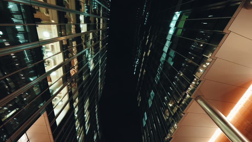 Low angle dolly shot illuminated skyscrapers cityscape at night, financial district looking up modern architecture office buildings, city business center downtown, gimbal shot, Warsaw evening street