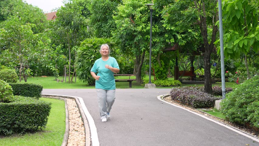 Senior woman jogging in outdoor stadium. Elderly female person is happy about cardio for health and wellness while walking or running in summer. Concept of healthcare and active lifestyle for healthy Royalty-Free Stock Footage #1111242335