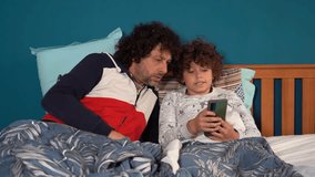 Father and son boy child 9 years old watching smart phone on line internet on the bed in bedroom before follow asleep - unhealthy habit and Internet addiction in childhood - Powered by Shutterstock - Get 15% off with code: PIKWIZARD15