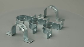 Metal clamps rotate on a gray background. Metal clamps for fastening thin pipes.
