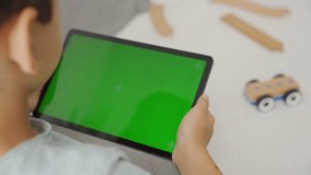 Kid boy gaming or using social media on tablet with chroma key background. Child holding ipad with green screen not interested in wooden toy car - Powered by Shutterstock - Get 15% off with code: PIKWIZARD15