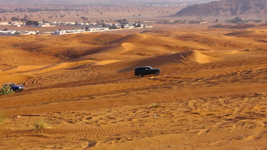 4x4 cars dune bashing, driving up the sand dune in the Fossil Rock desert with mountains in the background, Sharjah, United Arab Emirates.