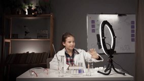 Studying chemistry. Child blogger wearing white lab coat studying chemistry making video of experiment
