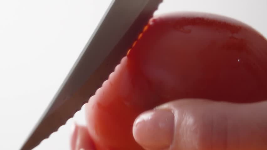 Fingers scoring and peeling the skin from a bright red tomato.