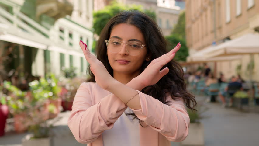 Female portrait young Indian Arabian ethnic woman showing prohibition sign serious businesswoman crossing arms refuses gesture no stop negative shaking head dissatisfied protests outside city street