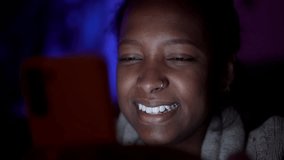 Close up of beautiful young African American woman happy at night using her mobile cell phone for social media. Cheerful black generation z girl face laughing scrolling addicted to networks indoors. - Powered by Shutterstock - Get 15% off with code: PIKWIZARD15