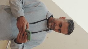 Vertical video, Middle-aged man in sportswear typing an SMS message on his mobile phone after training
