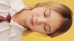 Vertical video, Young woman dressed in shirt and tie opens her eyes looking at camera with smile isolated on yellow background in studio