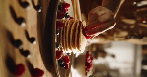 Unknown woman decorates pancakes with berries and sprig of mint. Cinematic vertical video for advertising, beautifully decorated table. Homemade food and comfort concept. Treat for eyes and taste bud