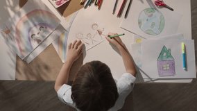 Boy at desk, skillfully painting picture of his family and vibrant rainbow. Drawing reflects happiness and love present in harmonious family. Heartwarming image of his family, dream about happiness