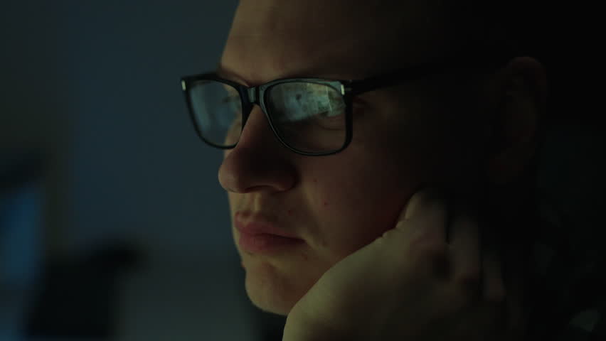 A man with glasses works at a laptop computer at night. This IT professional is deeply concentrating on the information that flashes on the screen, with a serious look on his face Royalty-Free Stock Footage #1111259287