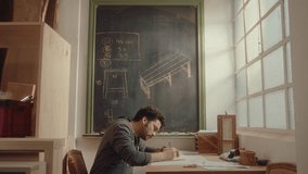 Side view of young woodworker sitting at desk near the window, drawing sketches of furniture design during day in carpentry workshop - Powered by Shutterstock - Get 15% off with code: PIKWIZARD15