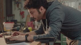 Professional woodworker leaning on workbench, surfing the Internet on laptop and drawing furniture sketches in woodshop. Side view, medium shot - Powered by Shutterstock - Get 15% off with code: PIKWIZARD15