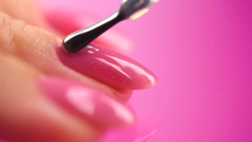 Applying Nail polish, pink shellac UV gel, varnish, manicure process concept in beauty salon. Transparent top coat drop on brush. Over pink background. Application of nail polish close up Royalty-Free Stock Footage #1111260571