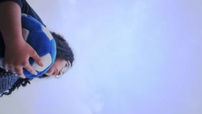 Vertical video of woman holding blue soccer ball and using vuvuzela to support team in cloudy day