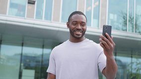African American man holding smartphone having video chat on urban street in city. Guy blogger chatting with best friends in social network. Man having virtual meeting online chat video call outdoor