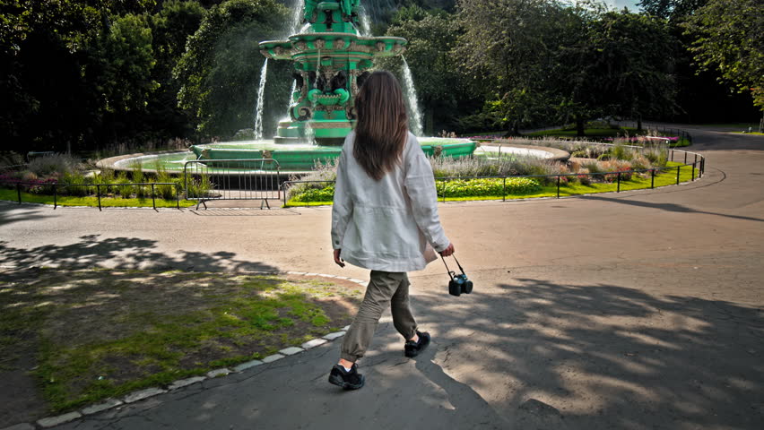 A beautiful woman visits Ross Fountain in Edinburgh, Scotland. Tourist girl looking at the Garden-side, cast-iron fountain representing science, arts, poetry and industry with Edinburgh Castle.
