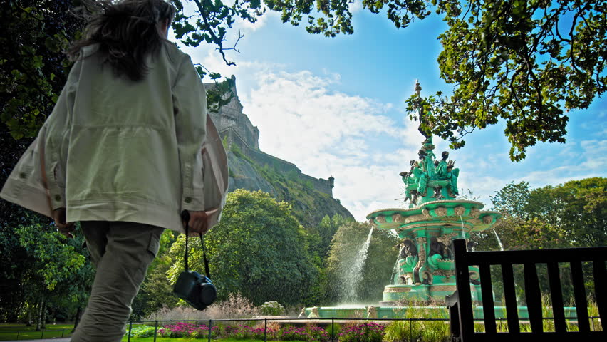 A beautiful woman visits Ross Fountain in Edinburgh, Scotland. Tourist girl looking at the Garden-side, cast-iron fountain representing science, arts, poetry and industry with Edinburgh Castle.
