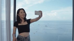 Asian woman in hotel near sea using smart phone cheerful selfie or take a photo or video call.