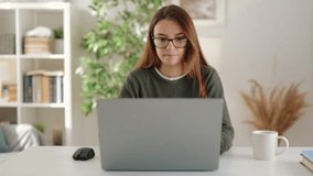 Joyful young businesswoman captured in portrait while engaging in remote work from cozy and comfortable apartment, using laptop