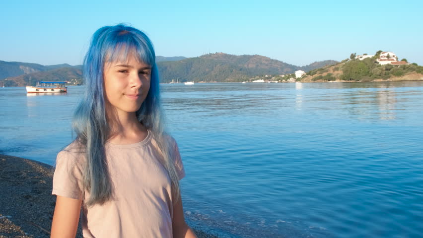 Blue sincere girl on shore. A nice sincere girl with blue hair put her hands on heart to admire the lake view during summer vacation.