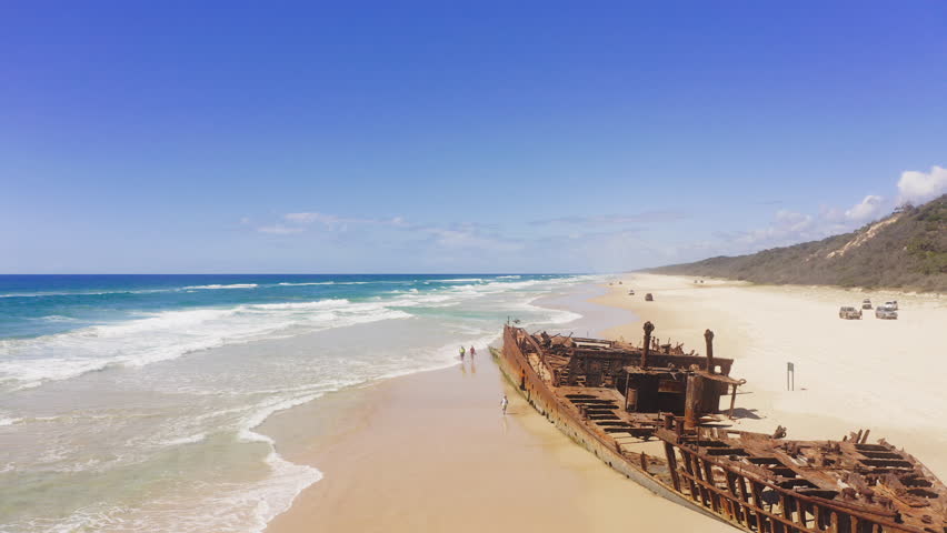 Drone, shipwreck and beach with people on sand for traveling, vacation and adventure on Fraser Island. Person, together and holiday for summer with walk on shore to check, explore or inspect site