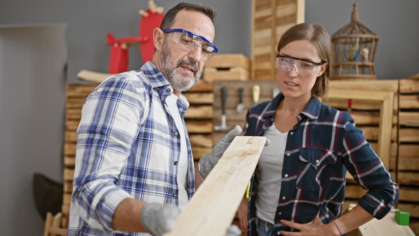 Two dedicated carpenters speak serious shop, holding lumber plank in indoor carpentry business