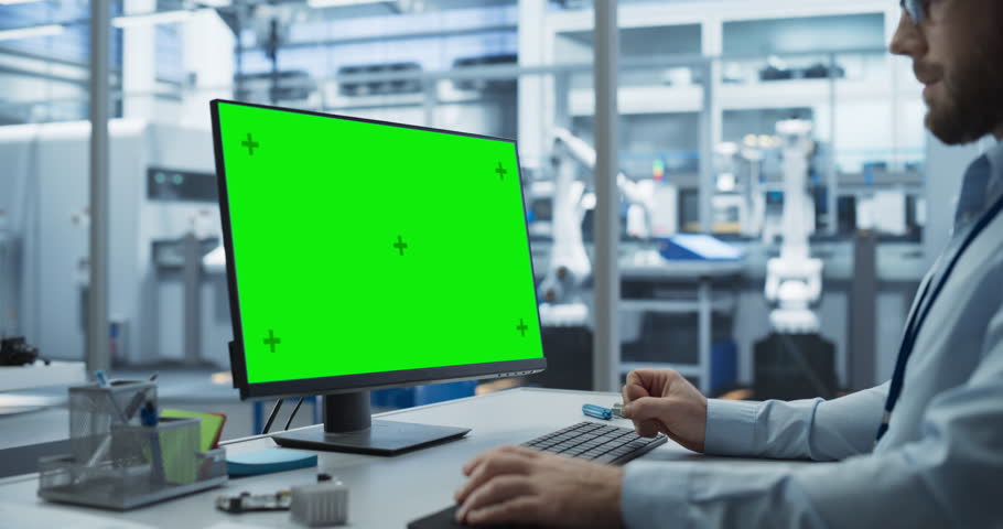 Young Industrial Software Engineer Working on a Desktop Computer with Green Screen Mock-Up Display. Modern Factory with High-Tech Machinery and Robotic Arms in the Assembly Hall Royalty-Free Stock Footage #1111285897