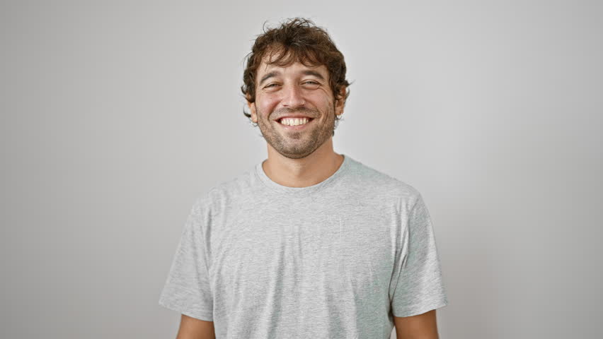 Cheerful young man flashes a cool, confident smile while wearing a casual t-shirt, a proud expression radiating joy from his face, standing isolated on a white background.