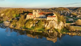 Tyniec near Krakow, Poland. Benedictine abbey, monastery and church on a steep rocky cliff and its water reflection in Vistula River. Aerial panning video in fall in sunset light