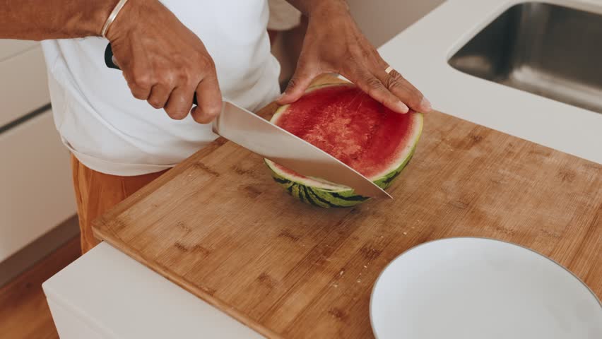 Closeup of hands slicing a ripe watermelon on a cutting board in the kitchen. Royalty-Free Stock Footage #1111296579