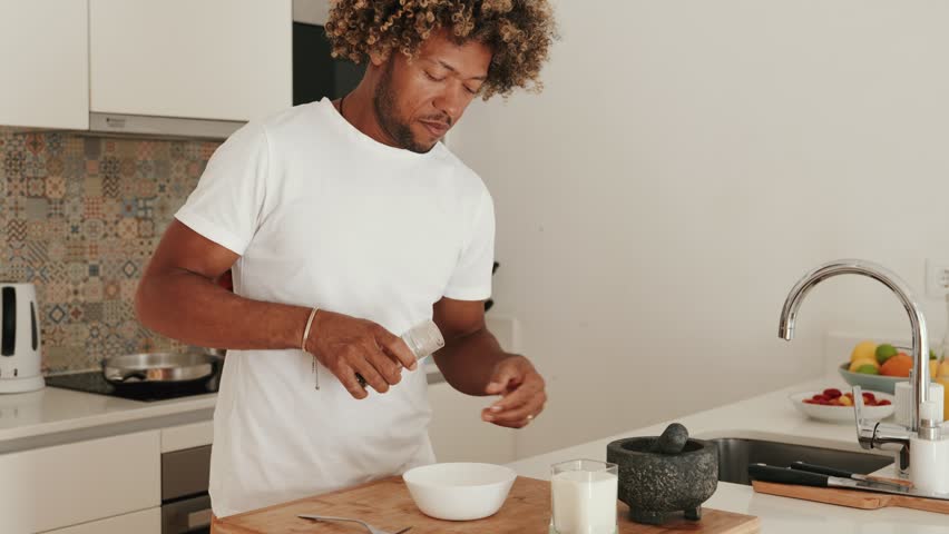Curly African male prepares breakfast, grinding pepper at home kitchen in the morning. Royalty-Free Stock Footage #1111296585