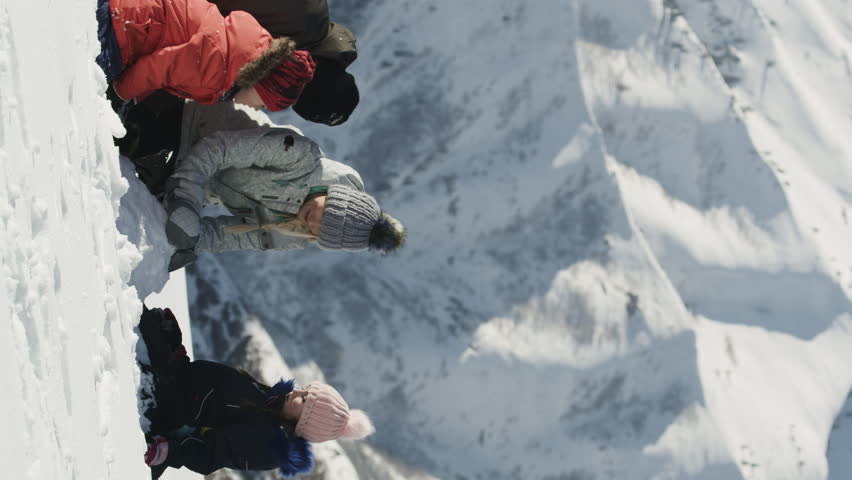 Tilt down to family kneeling in snow and building snowman near mountain - vertical video, south fork, utah, united states