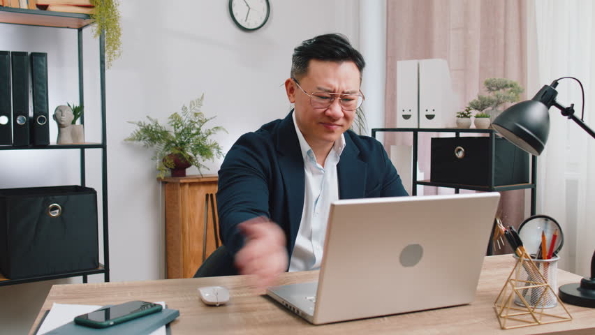 Irritated tired Asian business man while working on laptop, unexpected online website problem, computer virus data loss by hacking. Freelancer feeling mad about broken notebook at office workplace | Shutterstock HD Video #1111301695